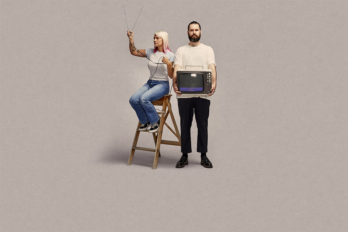 Man holding old fashioned TV, woman standing next to him holding antenna up